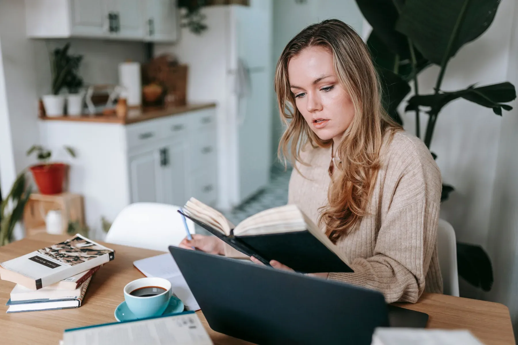 Frau liest ihre Notizen an einem Tisch mit Laptop und Kaffeetasse.
