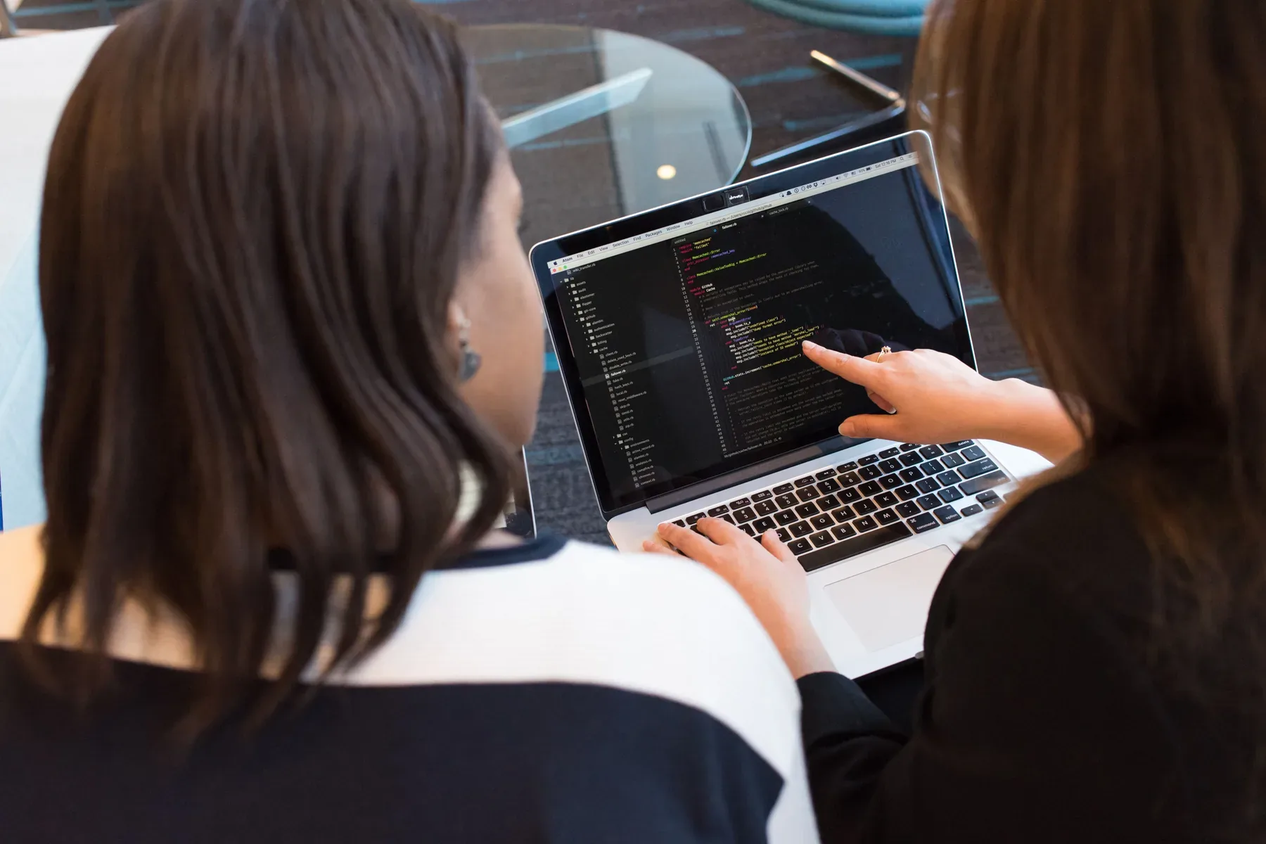 Zwei Personen prüfen gemeinsam Programmcode auf einem Laptop.